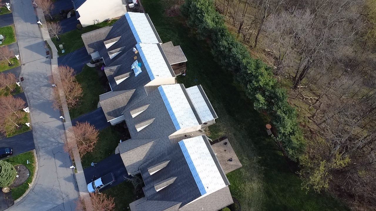 Top-down aerial of three townhome buildings with underlayment down and shingles in progress